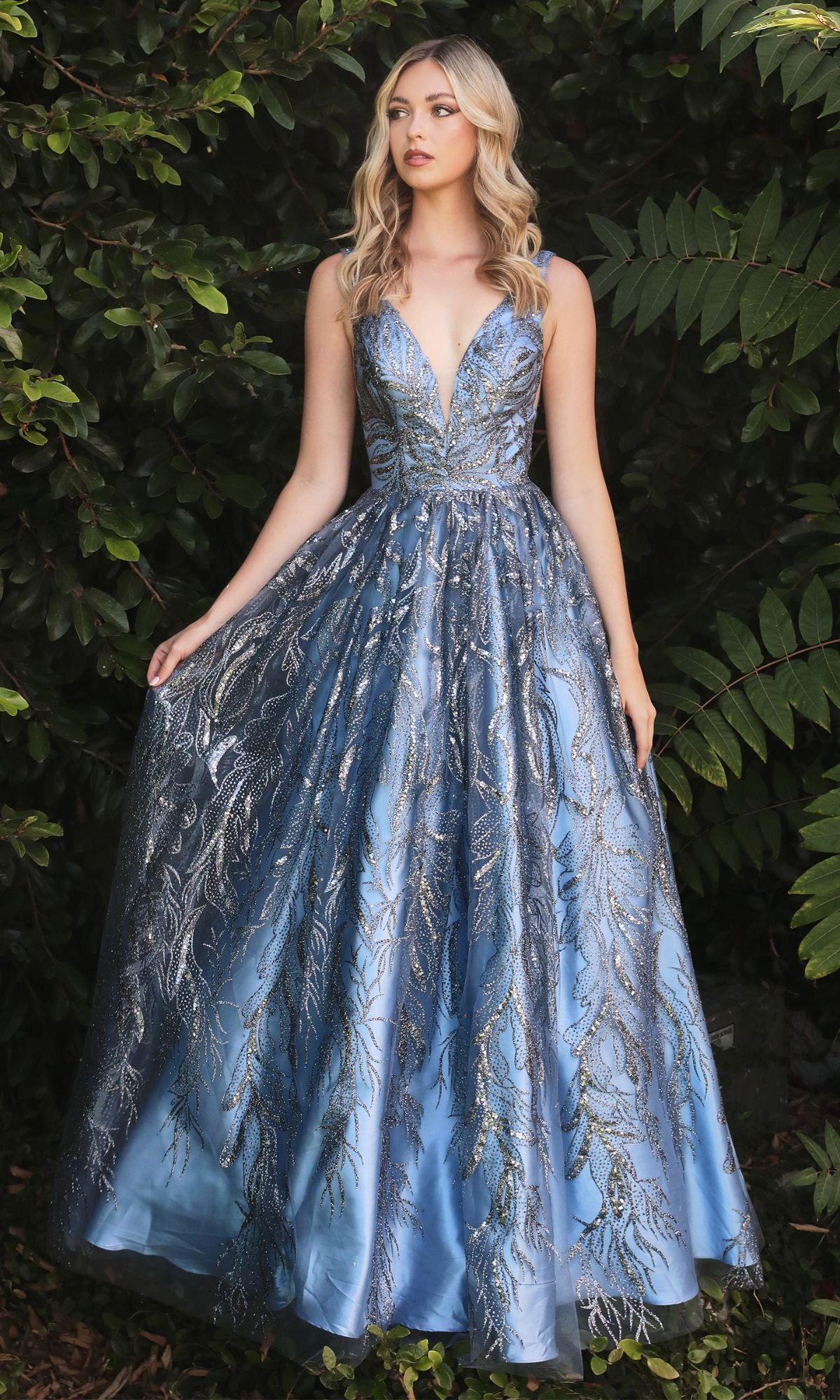 A woman wearing the Sleeveless Glitter-Print Long Prom Dress J812 stands outdoors in front of dense leafy greenery.